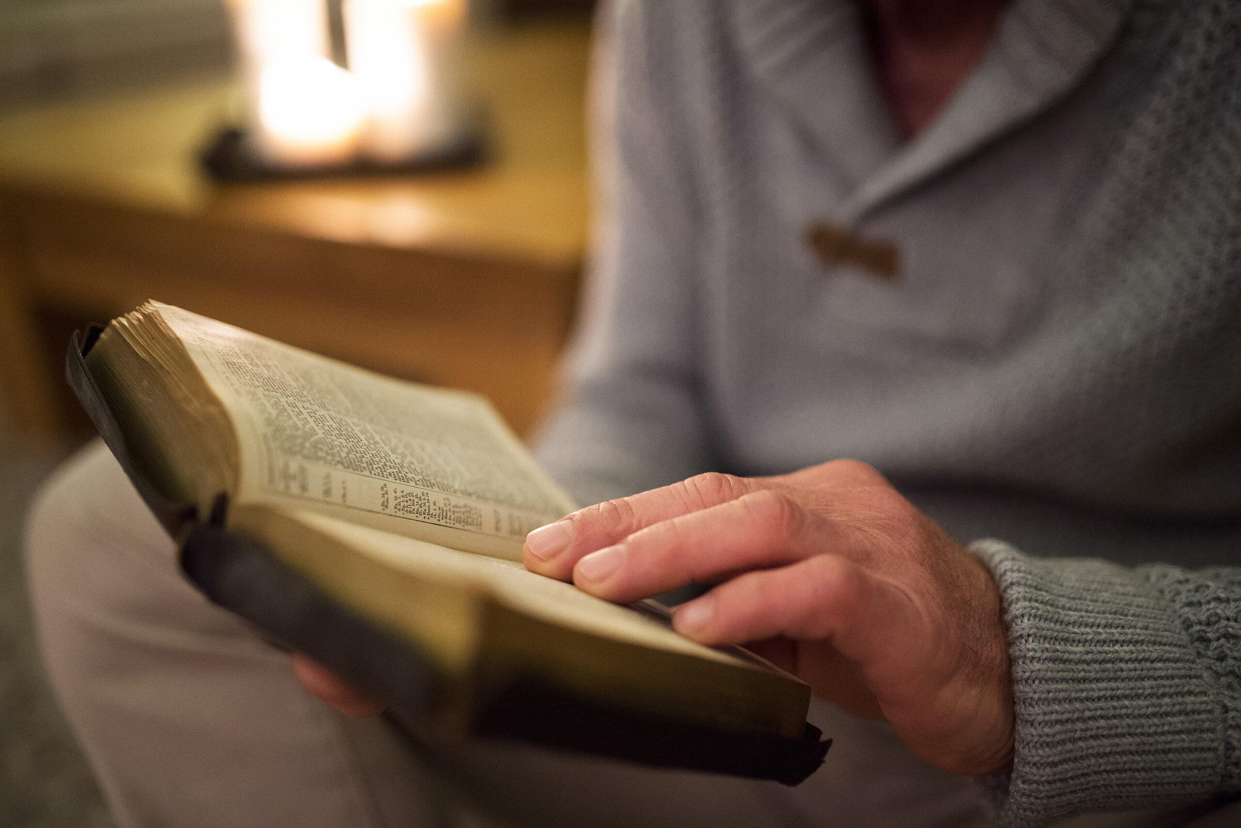 Unrecognizable man at home reading Bible, burning candles behind him